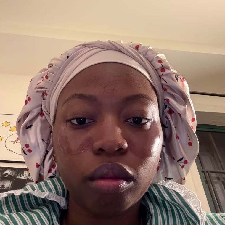 A person in bed with a cherry-print bonnet on and under-eye mask.