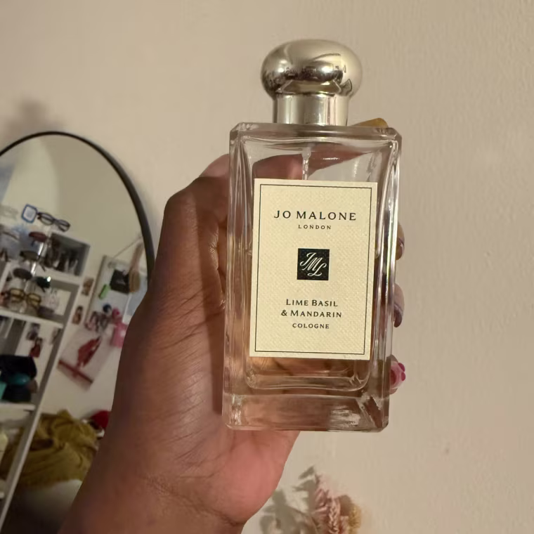 Photo of a fragrance in a glass bottle being held against a white wall