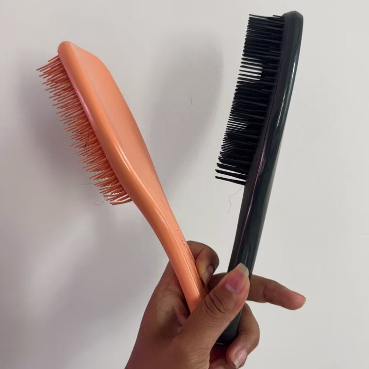 A hand holding the original Tangle Teezer and the new version for curly and coily hair