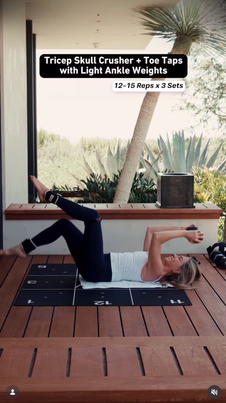 Jennifer Aniston does tricep skull crushers with alternating toe taps.