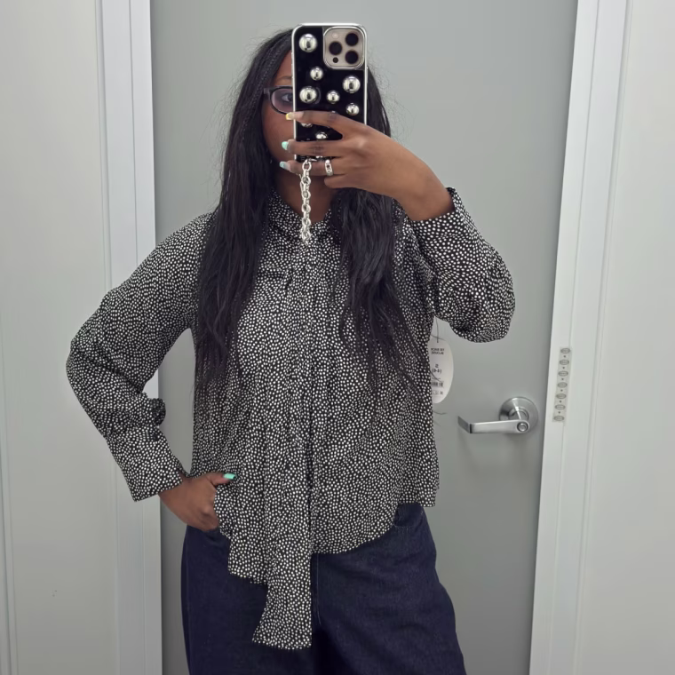 Mirror selfie of a woman wearing a long-sleeve blouse in a dressing room.