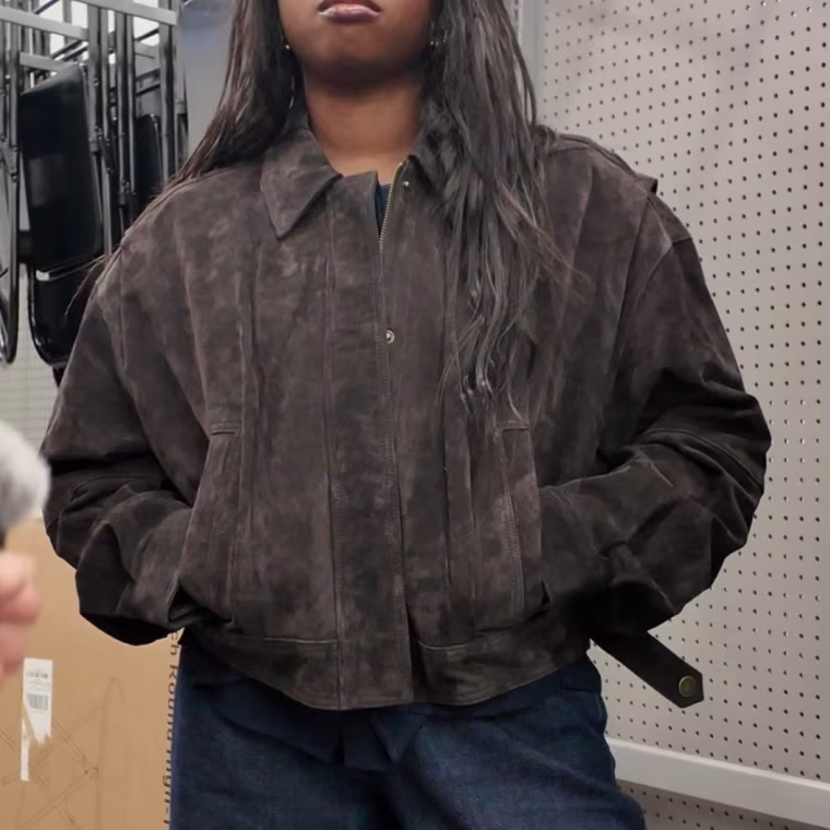 Photo of a girl with her hands in the pocket of a brown suede jacket.