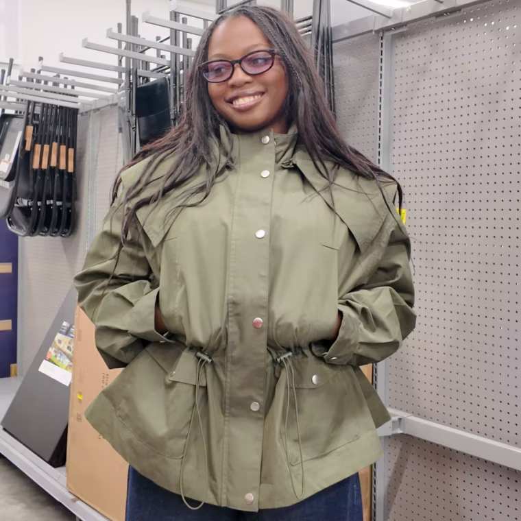 Photo of a girl smiling with her hands in the pocket of a green utility jacket.