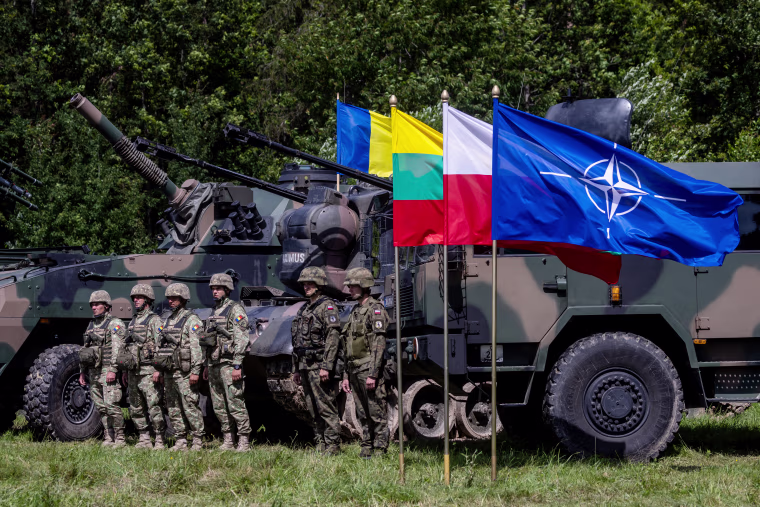 Six soldiers standing in front of camouflage military vehicles 