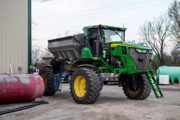 A worker refuels a fertilizer spreader with fuel