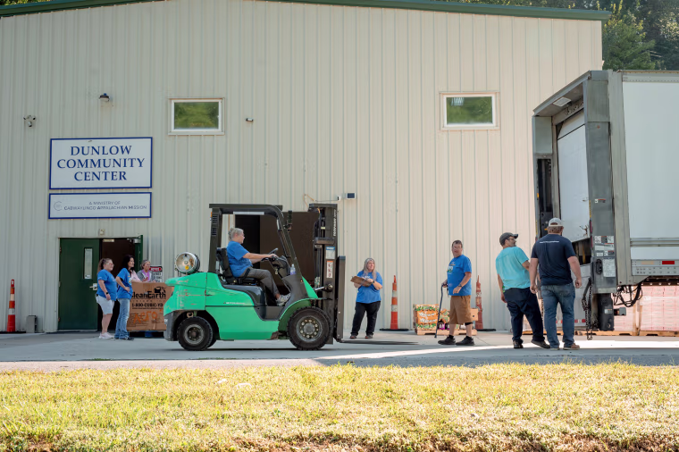 A longtime staff member operates the forklift to unload food, most of it purchased by Facing Hunger Foodbank. Bill Likens, center right, directed the food into position for the waiting cars.