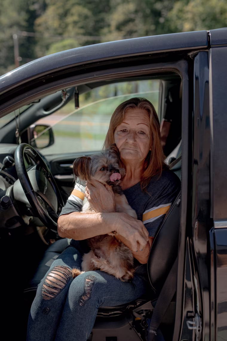 Joanne Girvin and her dog, Jasper, sat in line for several hours for a few boxes of food. Rising gas prices have cut into her grocery budget.