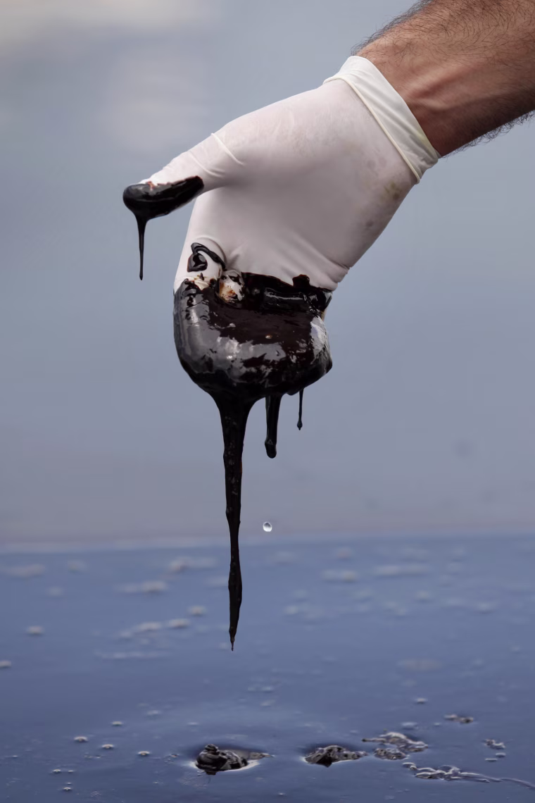 A hand wearing a white latex glove shows thick oil is pulled out of water surface.