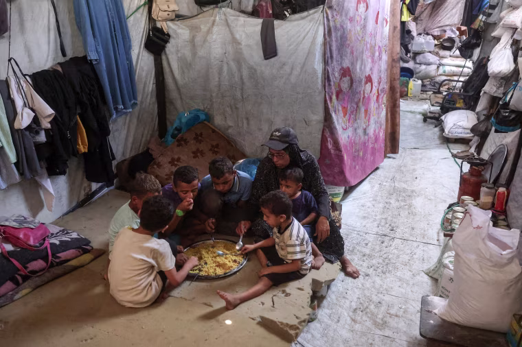Image: A woman shares a plate of food provided by a charity kitchen with her children at a camp in Khan Younis.