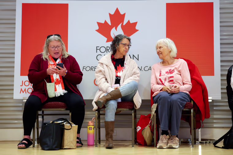 Image: Three women wearing Canadian flag clothing are sitting together.