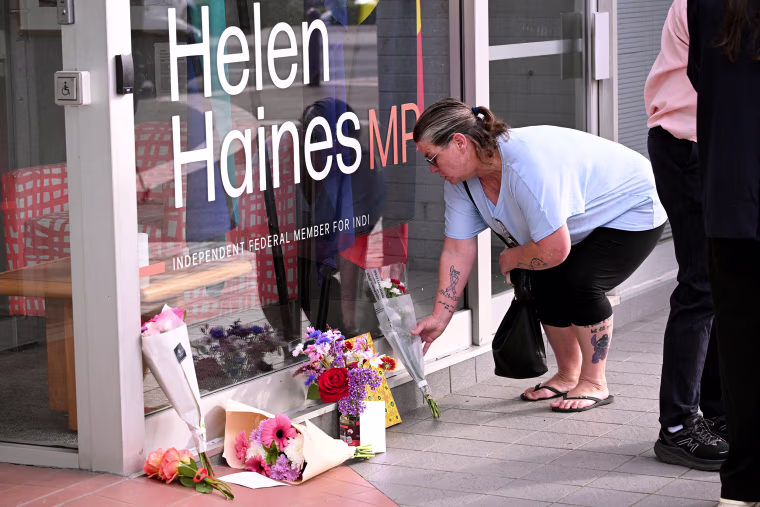 Image: A woman places flowers outside the office of Australian politician Helen Haines.