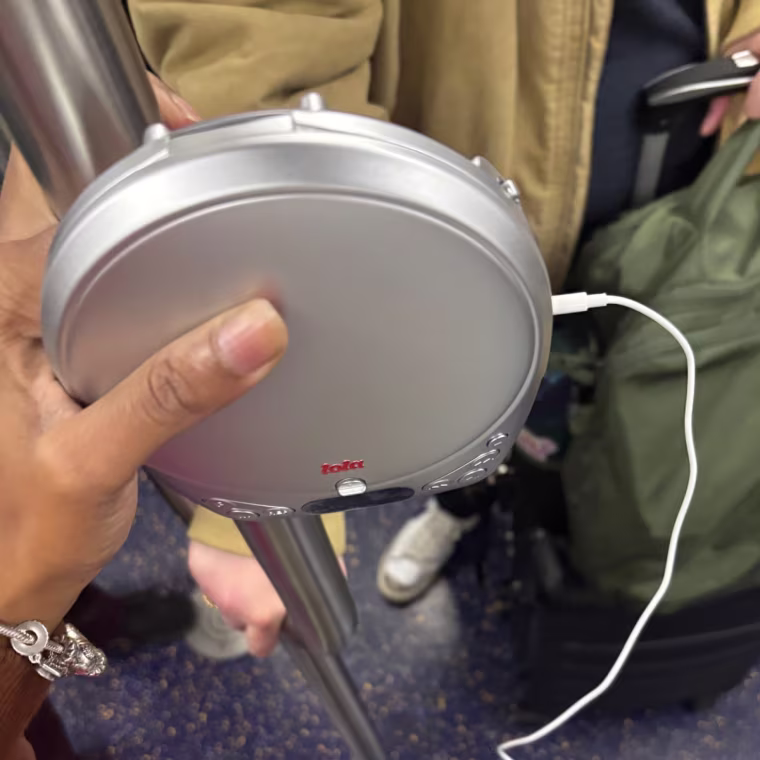 The Lola CD player being held against a pole on a subway train car.