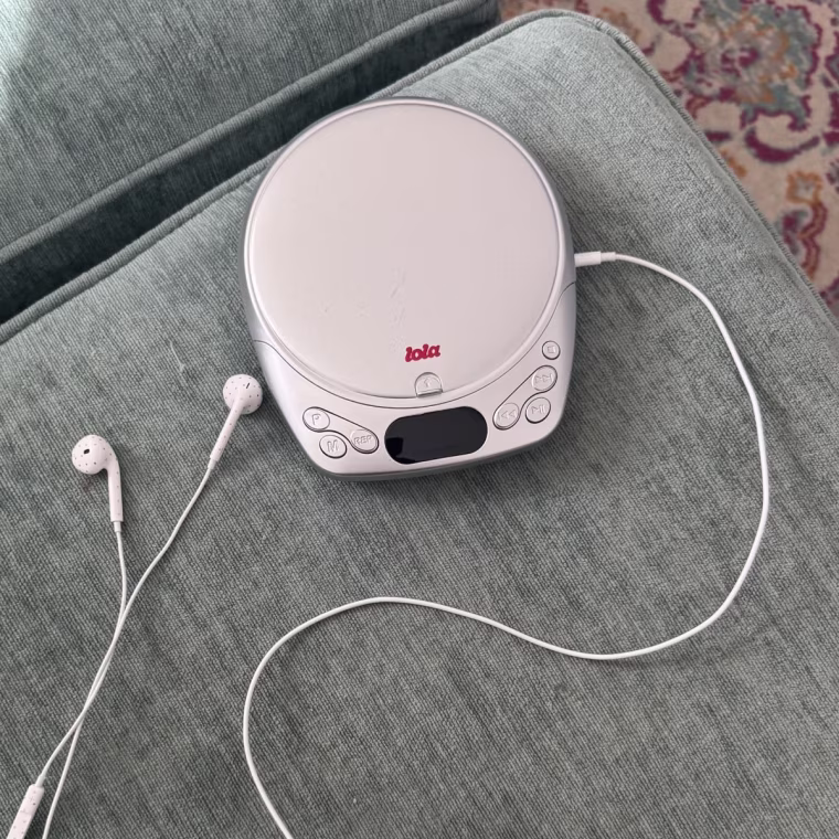 The Lola CD player from an aerial view on a gray couch cushion with a patterned carpet in the background.