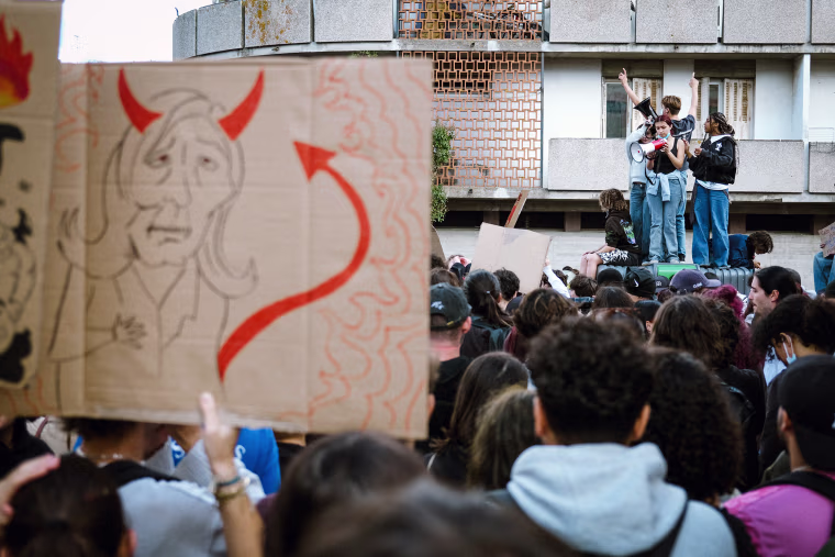 Image: High school students standing on a glass container holding a sign depicting Marine Le Pen as the devil during a protest.
