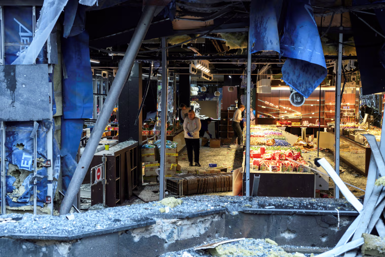 Image: A view through a smashed window of people clearing debris in a damaged shopping mall.