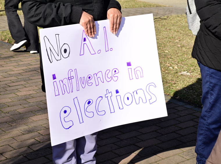 A person holding a sign that reads NO A.I. INFLUENCE IN ELECTIONS.