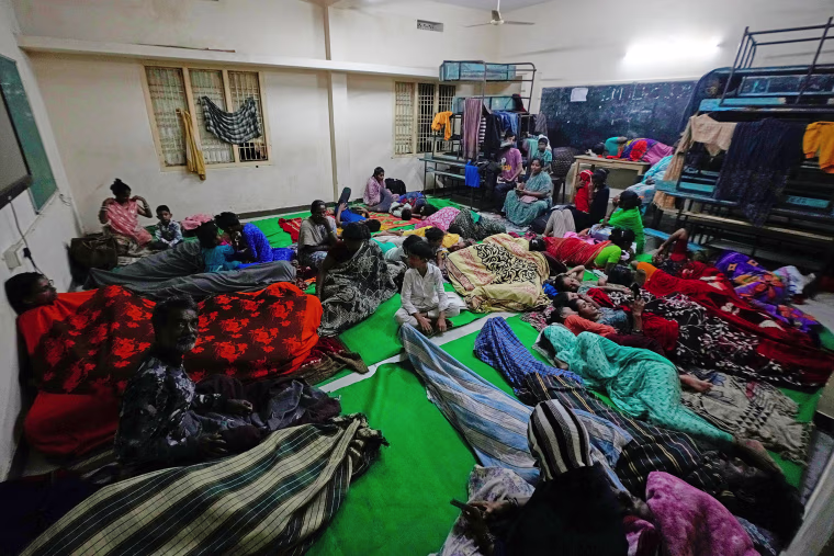 Image: People sit on the floor with blankets at a temporary shelter
