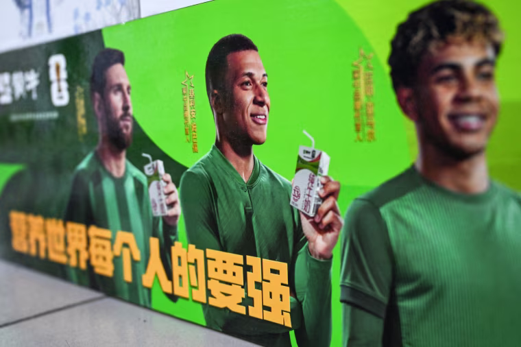 Image: An advertising billboard for Chinese dairy brand 'Mengniu' featuring football stars France's Kylian Mbappe (C), Argentina's Lionel Messi (L) and Spain's Lamine Yamal.