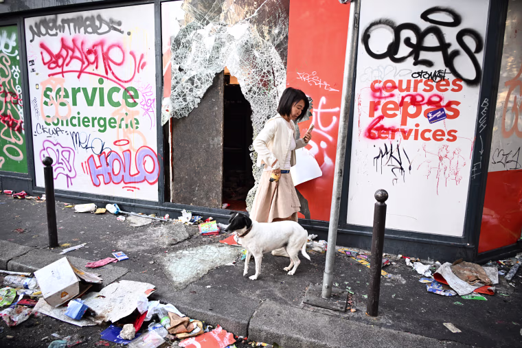 A woman walks her dog in front of a looted store, the day after a demonstration in Paris, October 18, 2026. 