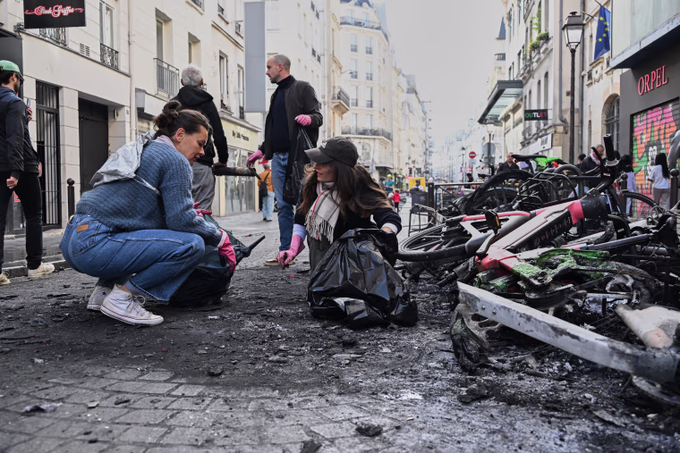 People clear debris on a street next to burned bicycles the day after a demonstration in Paris, October 18, 2026. 