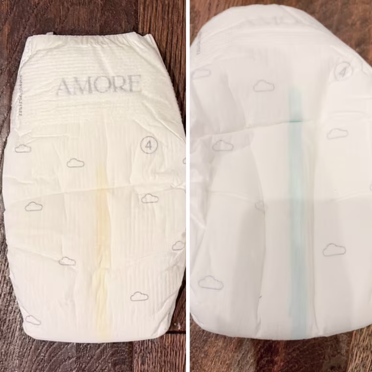 Side-by-side photos of a white Pampers AMORE size 4 diaper with a cloud print, showing a yellow wetness line on the left and a blue line on the right.