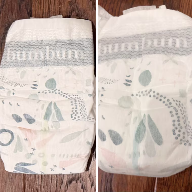 Side-by-side photos of a bumbum diaper with a soft abstract print, showing a pale yellow wetness line that turns light green-blue once wet.