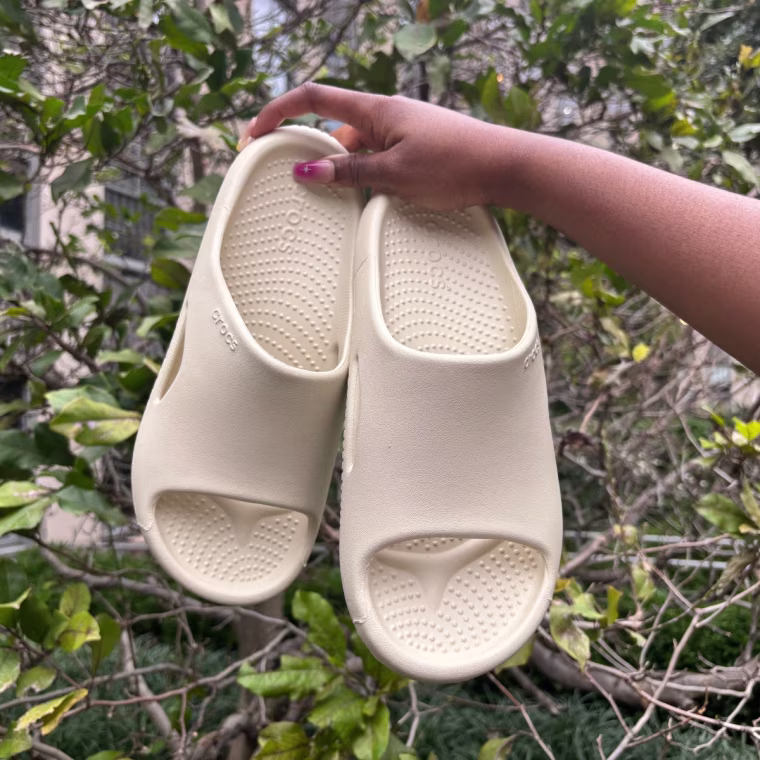 A person holding up a pair of Crocs Mellow Recovery Slides.
