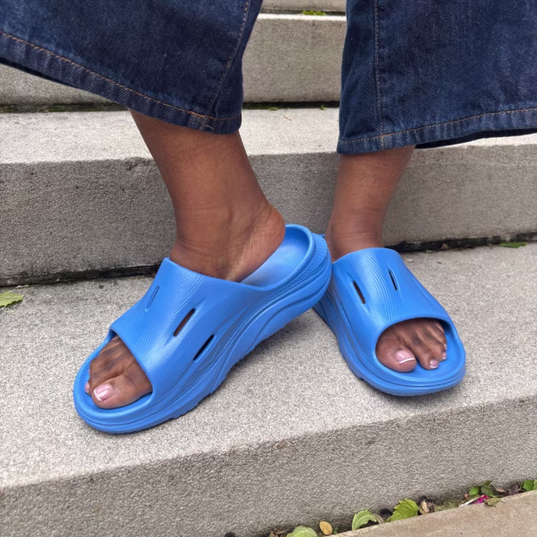 A person wearing a blue pair of Hoka Ora Recovery Slide 3s.