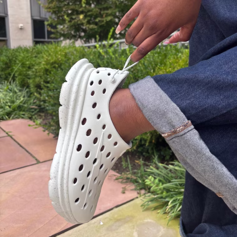 A person using the heel loop on the back of the Kane Revive sneakers to put them on their foot.
