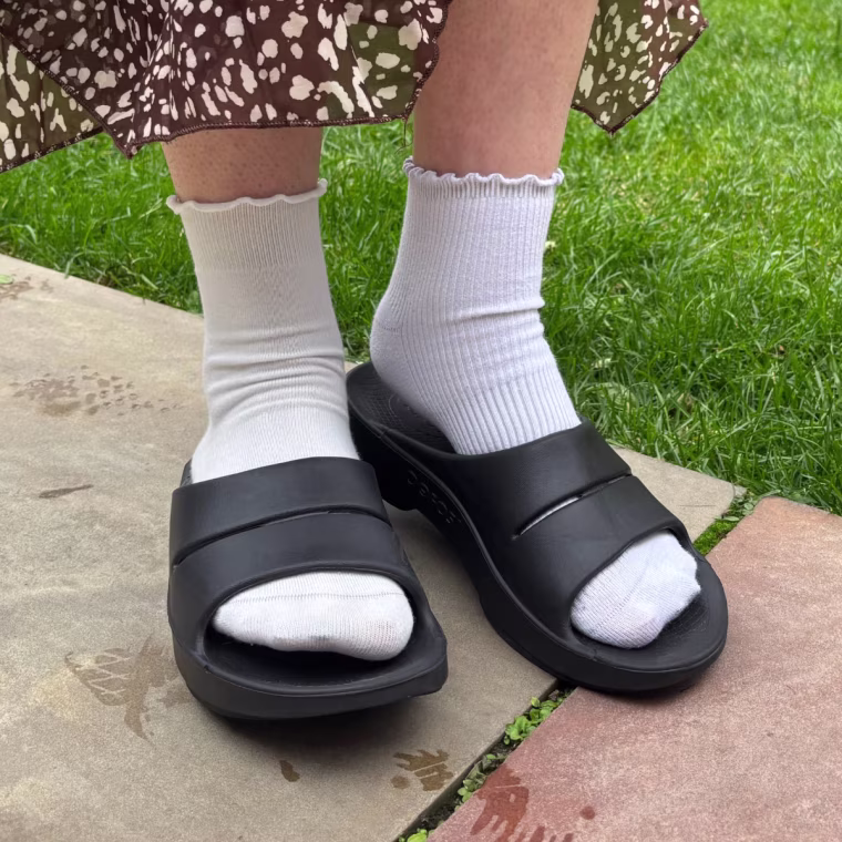 A person wearing the Oofos OOahh Slide in black.