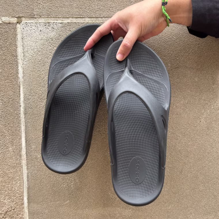 A person’s hand holding up a black pair of the Oofos OOriginal Sandal.