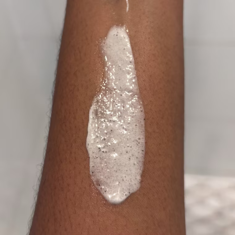 Cyklay Lactic Acid Foaming Body Polish spread onto a forearm in front of a shower.
