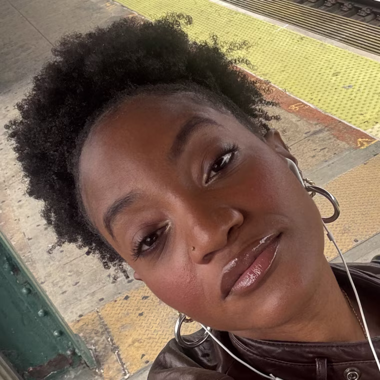 Morris taking a selfie photo from above wearing the Tower 28 lip gloss, in front of a subway track.