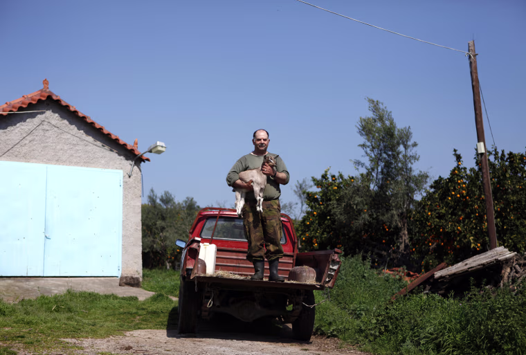 George Andrianakis, 56, a farmer, stands on the back of his pickup truck with one of his kid goats in the yard of his farm at the village of Stafania, in the Peloponesse area of Greece March 17. When asked how he had been affected by the economic crisis, Andrianakis replied,