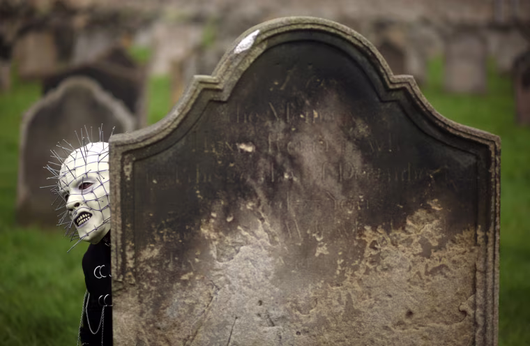A Goth peers from behind a gravestone.