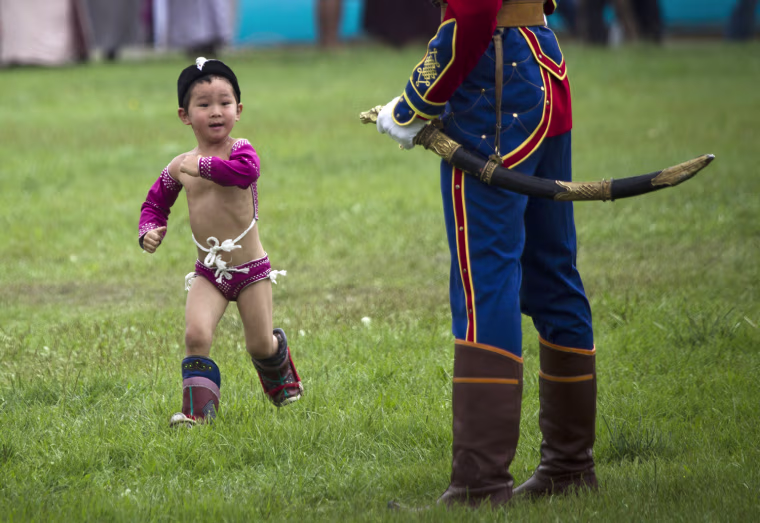 A Mongolian boy in costume runs past a member of guard of honor during the Naadam Festival in Ulan Bator, Mongolia Wednesday, on July 11.