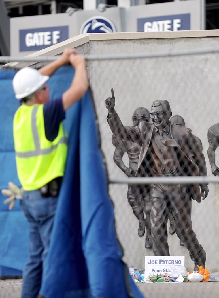 A worker hangs a blue tarp over the fence that was installed around the Joe Paterno statue. The university announced Sunday that it was taking down the monument in the wake of an investigative report that found that the late coach and three other top Penn State administrators concealed sex abuse claims against Jerry Sandusky, who was convicted last month of sexually abusing 10 boys, sometimes on Penn State's campus.