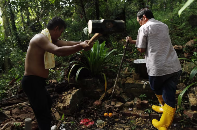 Mr Sim, left, breaks a tombstone with his sledgehammer as he exhumes a grave at Bukit Brown cemetery with his boss, Mr Leung.