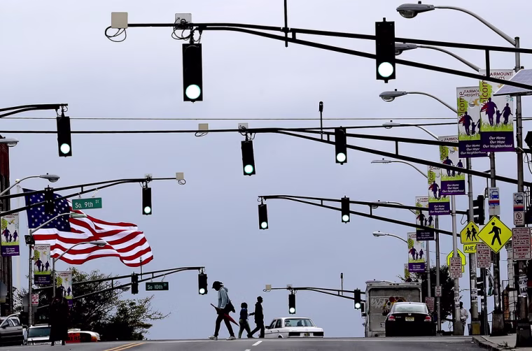 A U.S. flag waves in the wind as pedestrians cross the street in Newark, N.J.