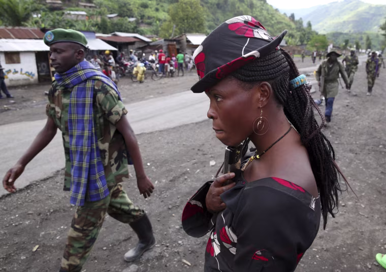 A M23 rebel fighter walks past a resident as they withdraw from the town of Sake in the Congo.