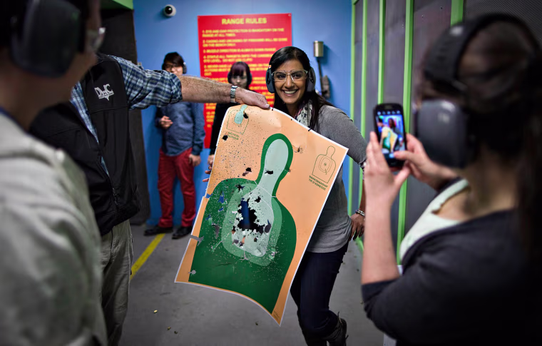 Mona Kambo, center, holds up her shooting target while her friend, Kylie Cronin, right, takes a picture at the DVC Indoor Shooting Centre where Friday night is 'Ladies Night.'