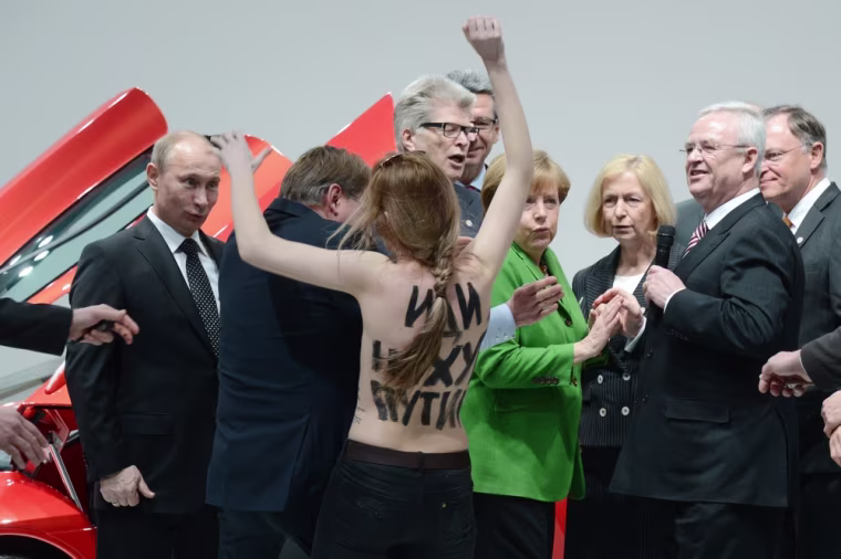 An eye-opening experience for Russian President Vladimir Putin (left) as he is confronted by a topless demonstrator during a tour of the Hanover Fair in Hanover, Germany, on April 8, 2013. He was accompanied by German Chancellor Angela Merkel (center right) and Volkswagen Chief Executive Officer Martin Winterkorn (extreme right).