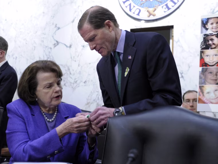 Senate Judiciary Committee member Sen. Dianne Feinstein, D-Calif., gets help with a green ribbon pin for the victims of Sandy Hook Elementary School, from fellow committee member Sen. Richard Blumenthal, D-Conn., on Capitol Hill in Washington, Wednesday, Feb. 27, 2013.