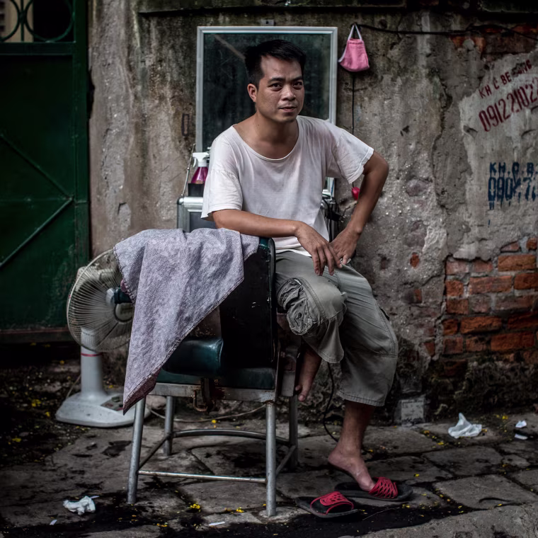 Thirty-four-year-old street barber Mr. Quy poses for a portrait as he waits for customers at his roadside barber shop on July 20, in Hanoi, Vietnam. Quy has been a street barber for more than 14 years.