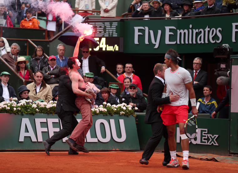 Rafael Nadal of Spain looks on as security guards restrain a protester after he lit a flare and ran on court before the start of a game in the Men's Singles final match.