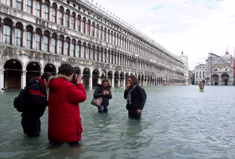 In this file photo, tourists take photos of each other in the flooded Saint Mark's square in Venice.