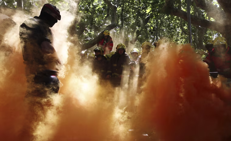 A police officer, left faces firefighters after a smoke bomb was set off during a protest against economy cuts in front of the Catalunya Parliament in Barcelona, Spain, Wednesday on May 29,.