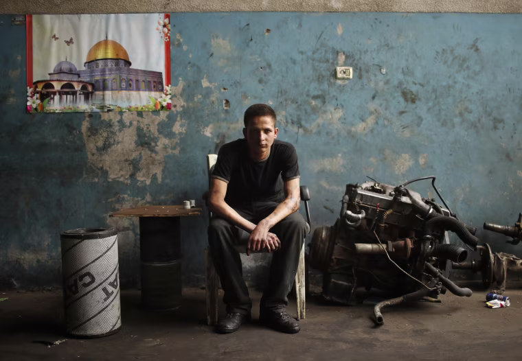 Palestinian Ali al-Batniji, 18, poses in an auto repair garage in Gaza City on May 30, 2013. A picture of the Dome of the Rock shrine and Al-Aqsa mosque in Jerusalem's Old City hangs in the background.