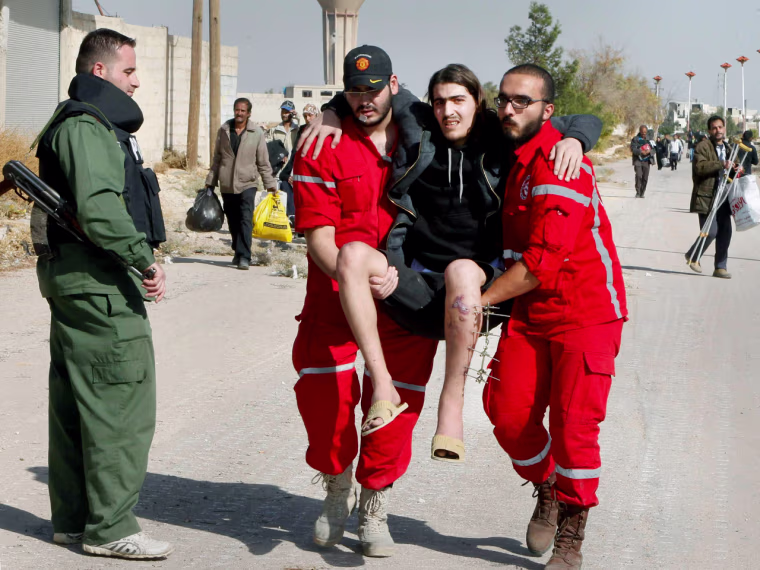 Volunteers from the Syrian Arab Red Crescent carry a sick man as Syrian families leave the besieged town of Mouadamiya.