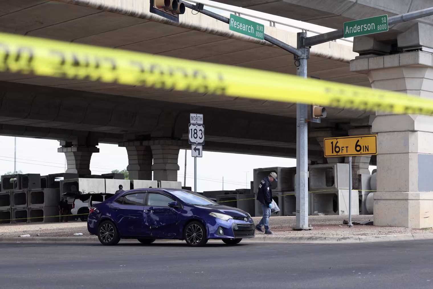 A dark blue Toyota car appears to have bullet holes while parked at an intersection behind yellow tape.